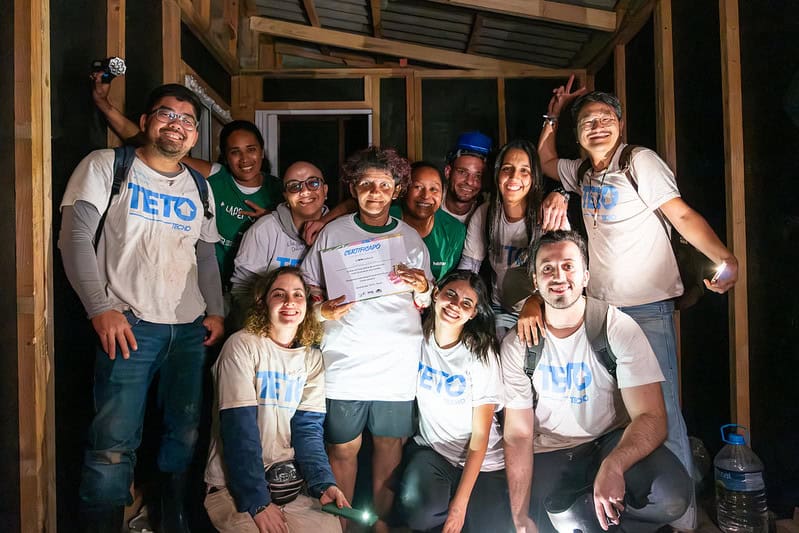 Moradora beneficiada no Jardim Lapenna segura certificado cercada por voluntários da TETO Brasil após a entrega de moradia.