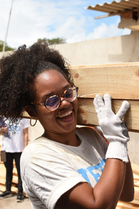 Jovem voluntária da TETO Nordeste sorri enquanto transporta materiais de construção 