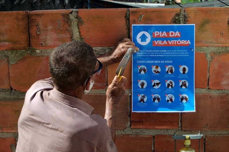 Homem prega cartaz sobre Pia para higienização em Vila Vitória 