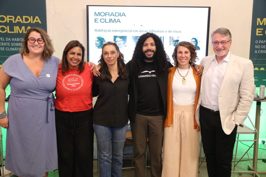 Camila Jordan e liderança comunitária Edith Vieira posam em pé ao lado de debatedores da mesa sobre emergência habitacional