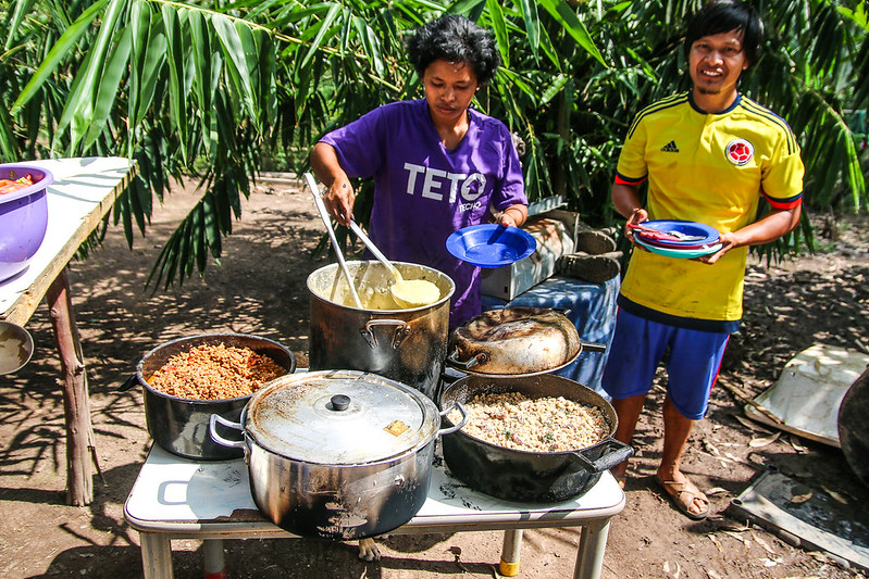 Indígenas de aldeia em São Paulo seguram pratos de comida em estação de alimentação