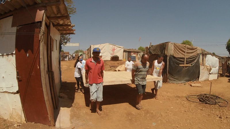 Foto de moradores de moradias precárias carregando materiais para construção