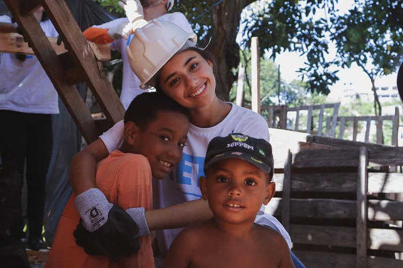 Voluntária abraça menino de comunidade impactada pela TETO. Ao lado dele, há outro menino.