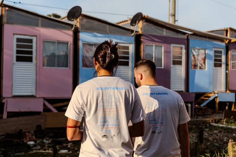 Voluntários da TETO caminham por comunidade com moradias recém-construídas, símbolo da atuação em territórios vulnerabilizados.