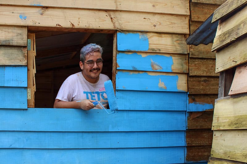 Voluntário da TETO pintando uma moradia emergencial durante ação em comunidade.