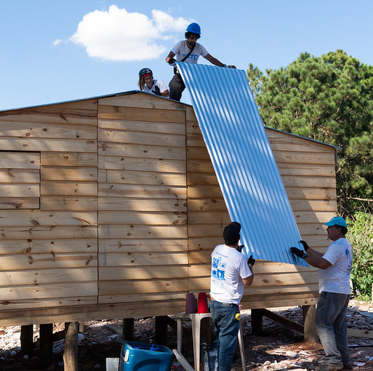 Voluntariado da TETO Brasil instala telhas na cobertura de uma moradia construída em uma comunidade.