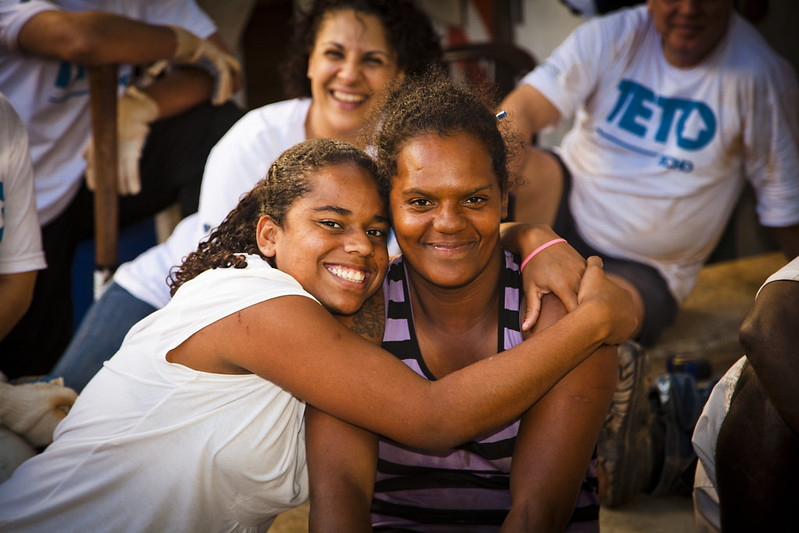 Moradoras de comunidade se abraçam e sorriem para a foto.